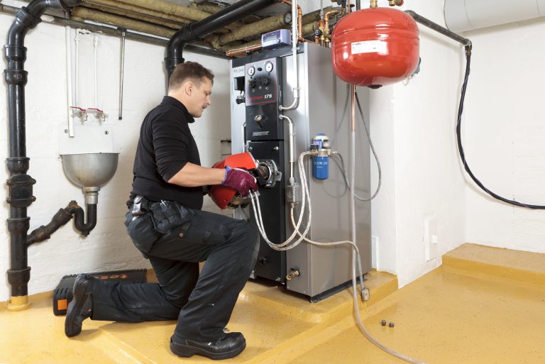 Nuori mies huoltaa omakotitalon öljylämmityslaitteistoa.